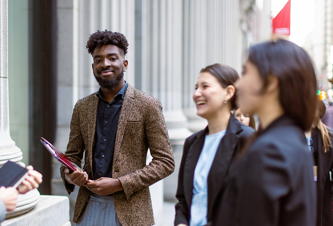 Two people in business attire smiling during a conversation outdoors.