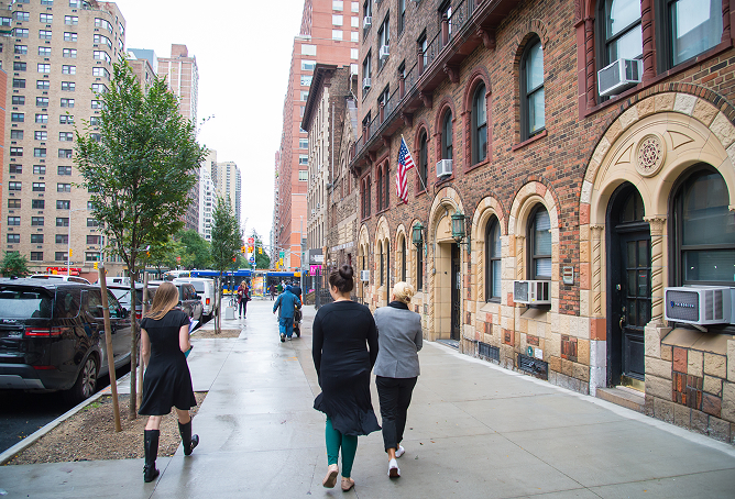 People walking along a New York City street beside a brick building.