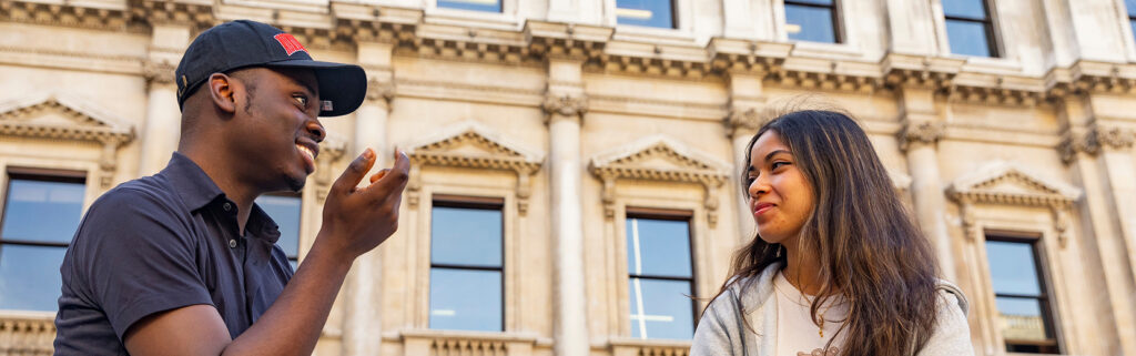 Two people smiling and talking outdoors in front of a classical building.