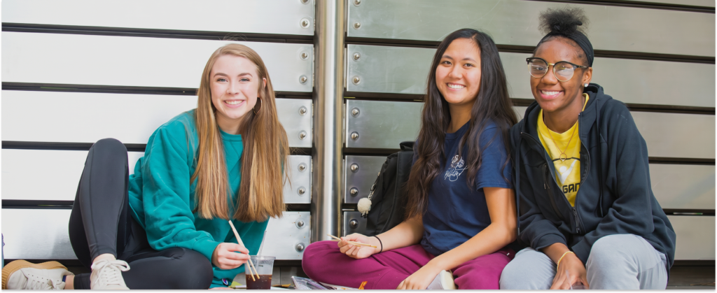 Three students sitting together on steps, smiling.